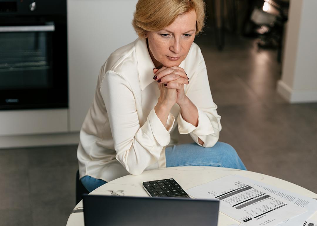 A middle-aged woman carefully looking at financial expenses from a laptop at home.