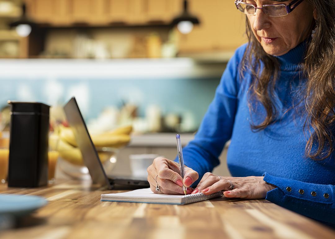 An elderly person writing a grocery list in a kitchen table.