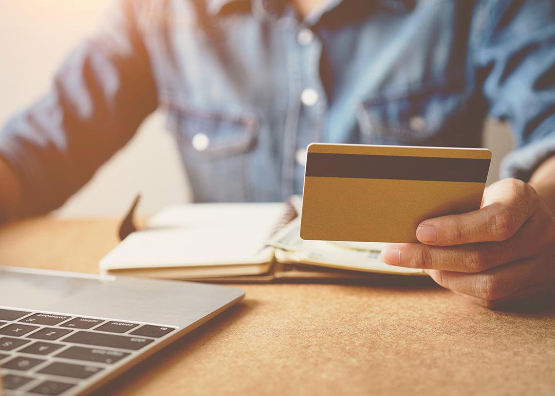 A person checking his credit card while reviewing finances from a laptop.