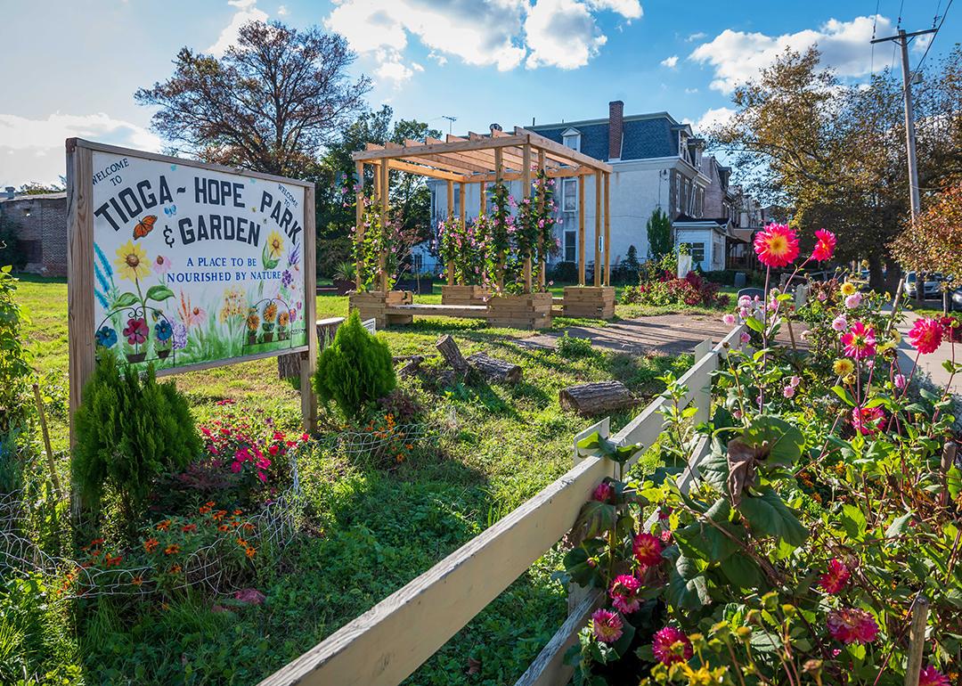 Roses bloom outside a fenced yard with a sign that says "Welcome to Tioga Hope Park &Garden."