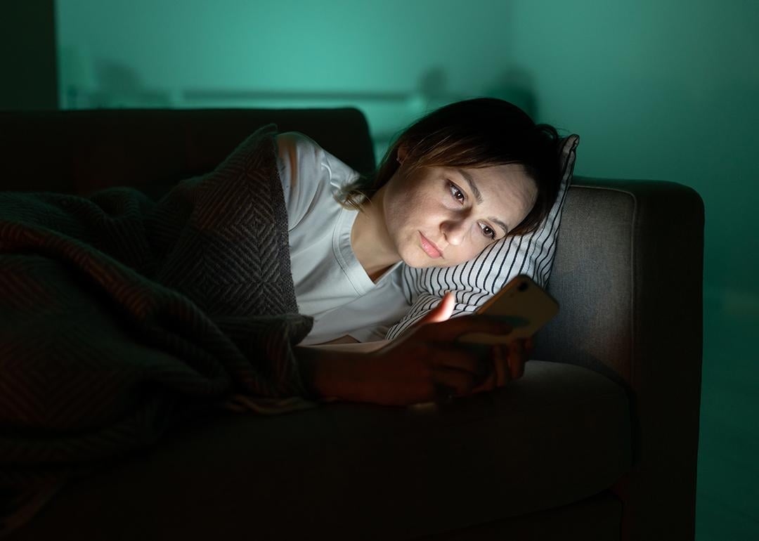 A person surfing internet from her smartphone in a dark room at night.