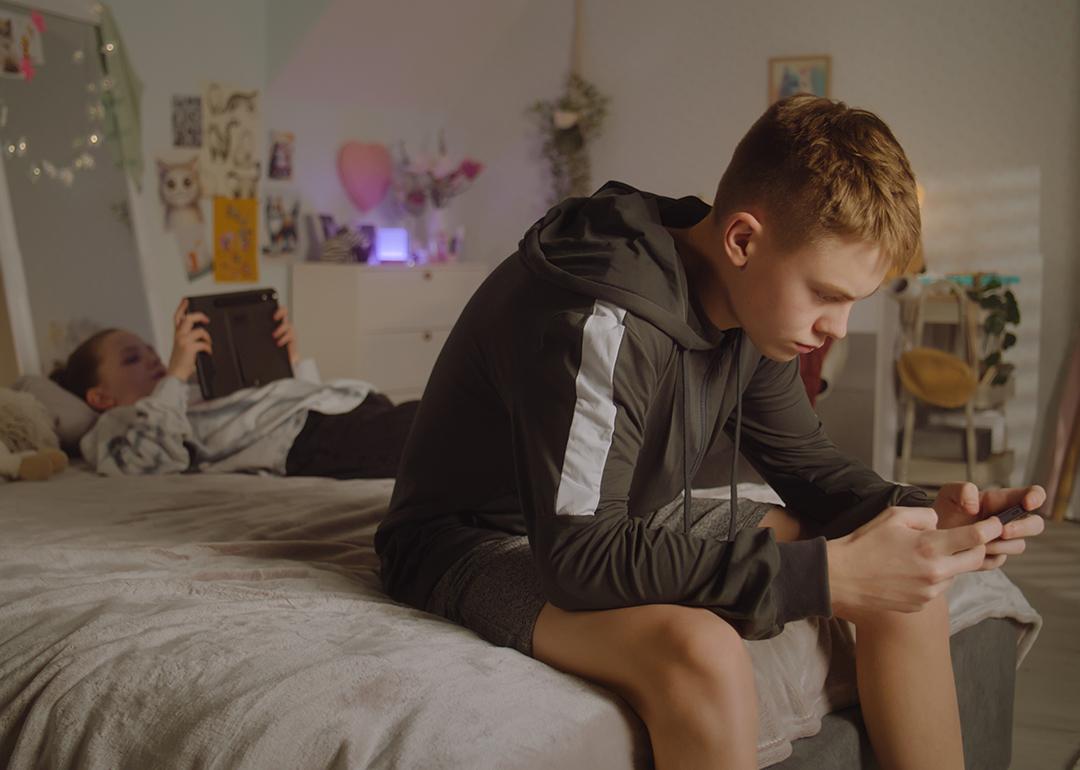 Teenage siblings at home scrolling through their phones.
