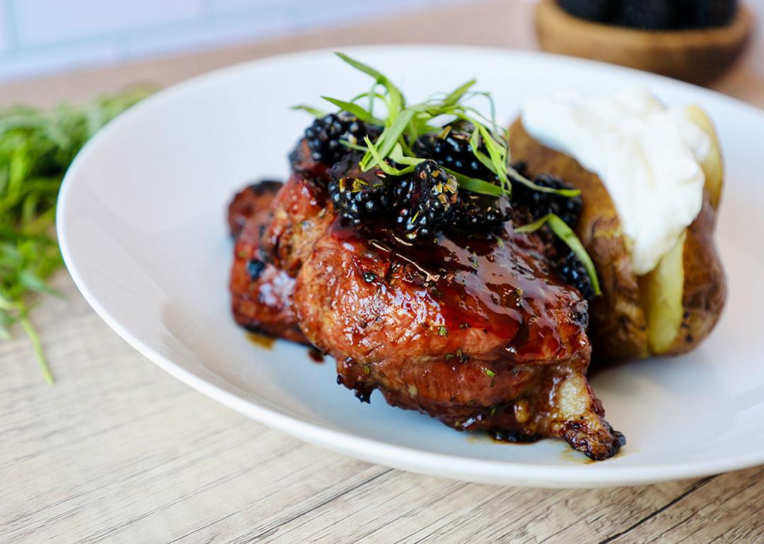A plate of savory grilled porkchop dish with berry sauce and potatoes.