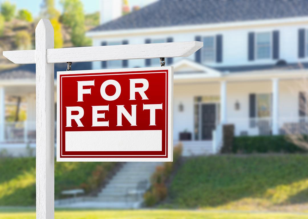 A For Rent sign placed in front of a residential house.