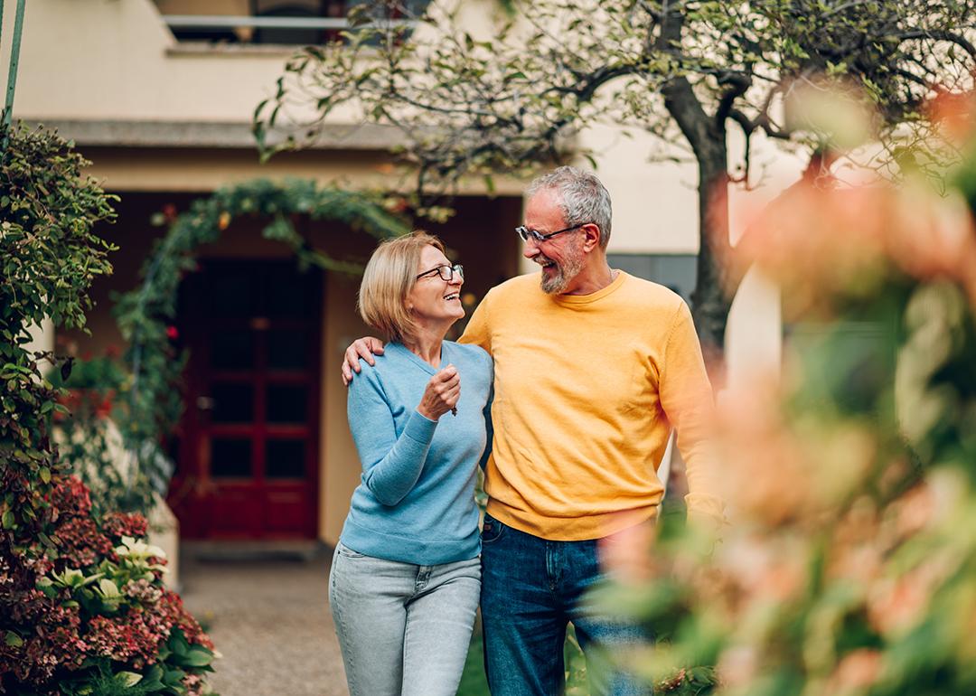 A senior couple happily standing in front of their new home.