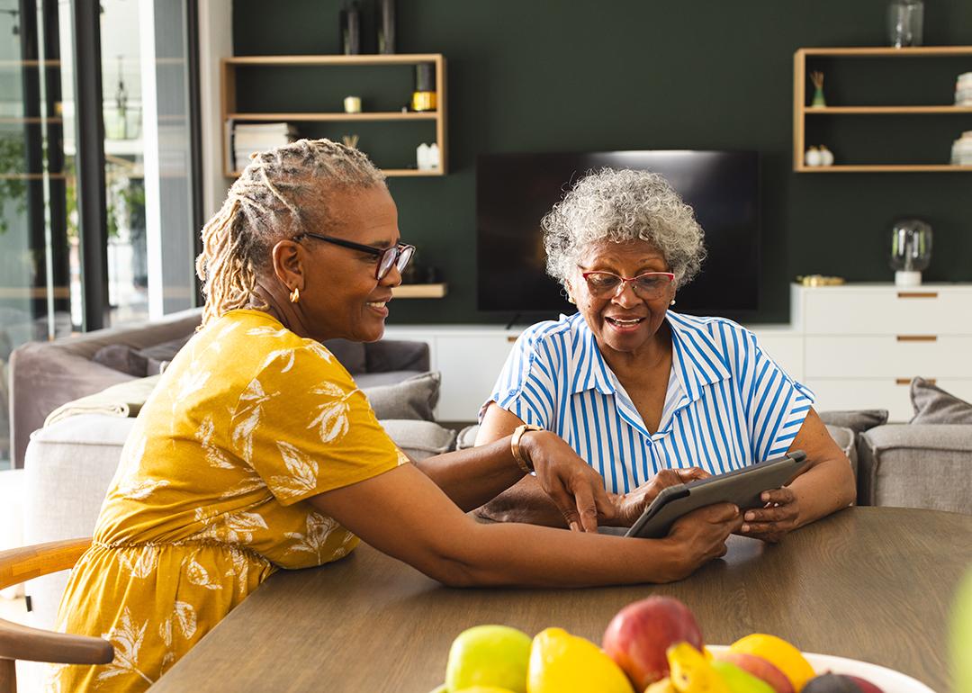 Two senior women sharing to use a tablet in their living room.