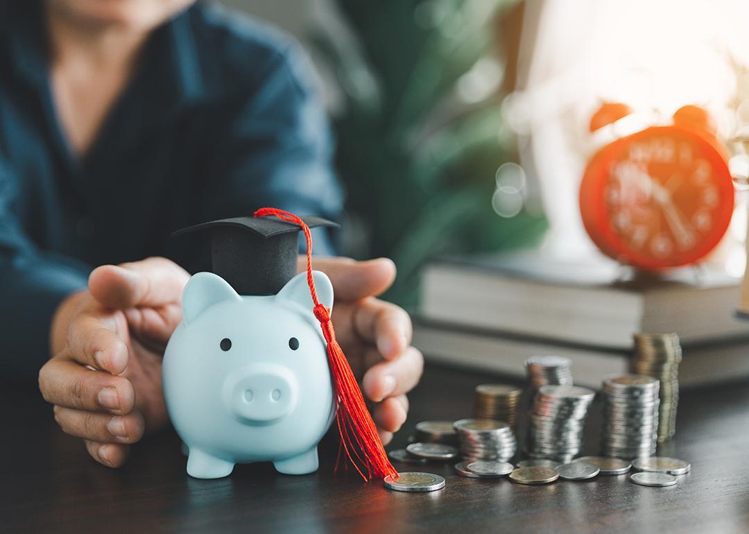 Person protecting a piggy bank with a graduation cap as a concept of saving money for education.