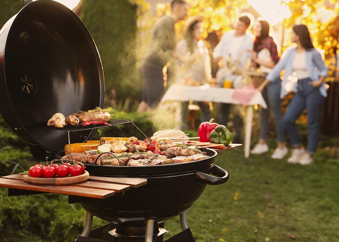 A focus on a barbecue grill set outdoors, with a group of friends having a party in the backdrop.
