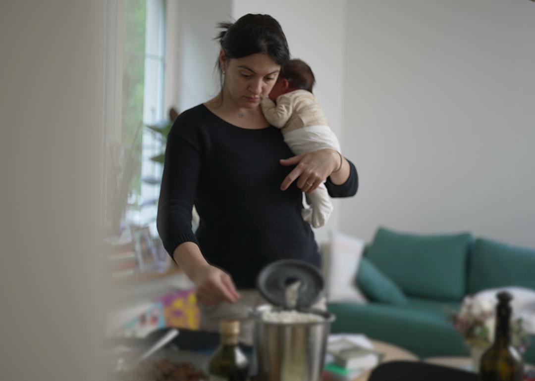 A mother holding her newborn baby multitasking at home.