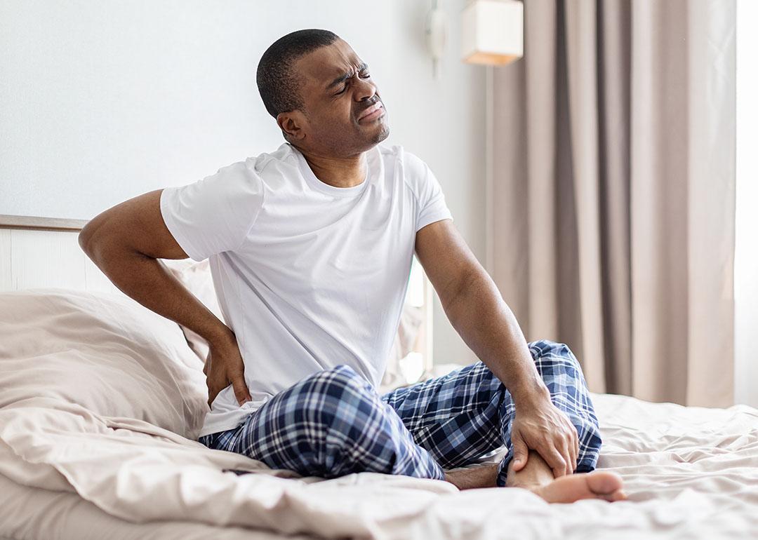 A man sitting on a bed experiencing lower back pain.