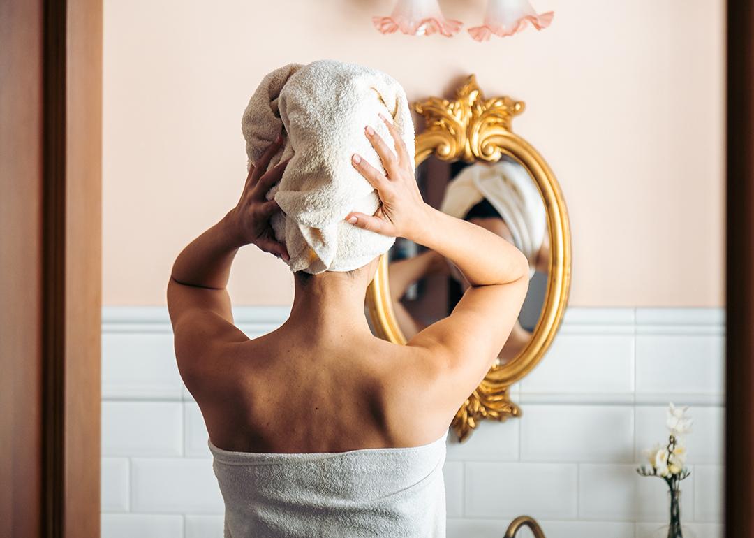 A person drying her hair in front of a mirror from a bathroom.