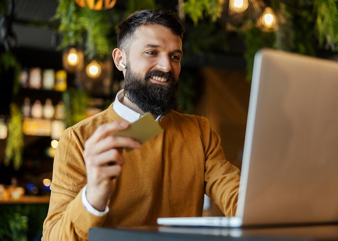 A man in a cafe happily holding a credit card while doing an online transaction.