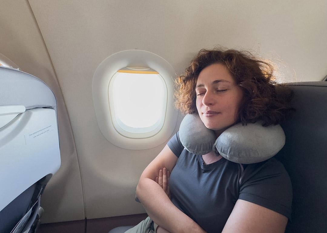 A person sleeping with a neck pillow from her seat in a plane.