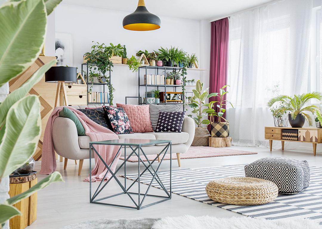 An interior of a spacious living room with plants, poufs, sofas, and cabinets.