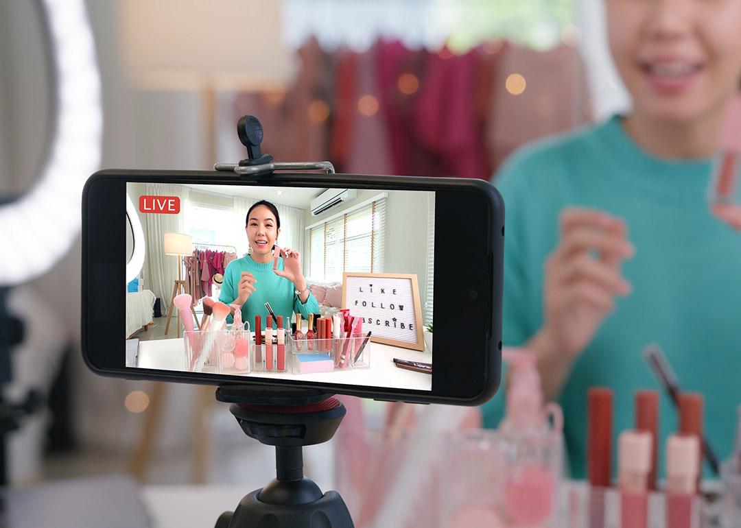 An online content creator reviewing cosmetic products live through a social media platform in her home studio.