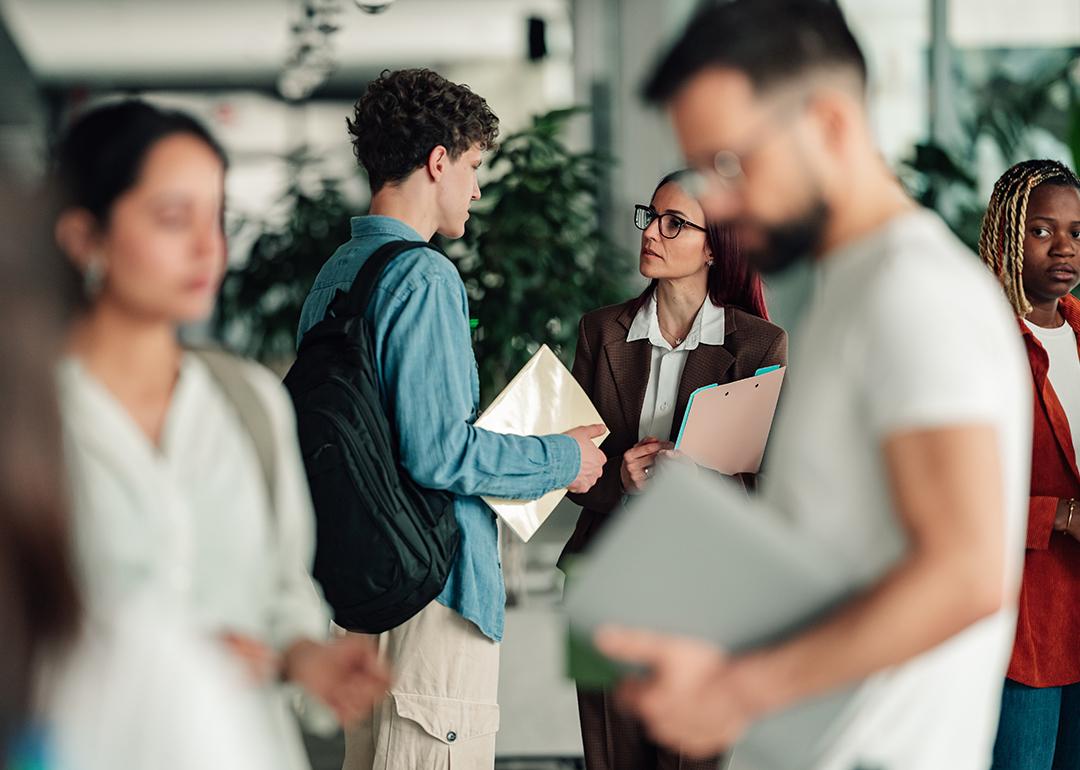A college student talks to a professor in a campus hallway.
