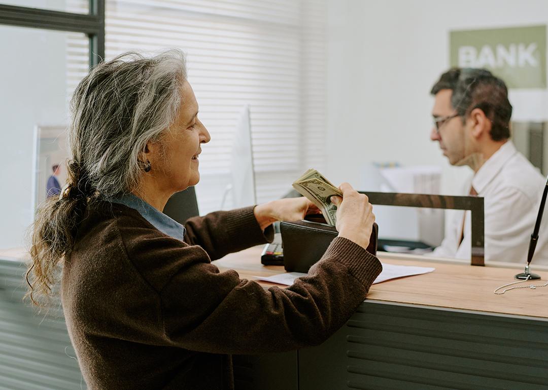 A senior woman handing money to a bank teller.
