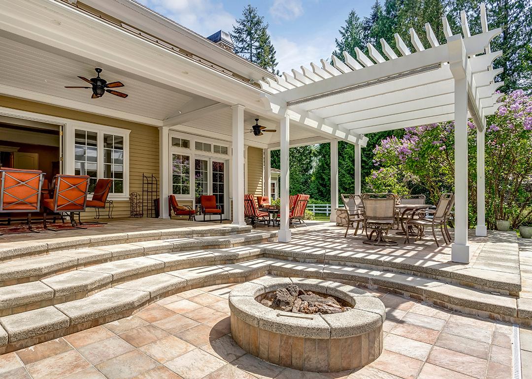 A modern luxury outdoor patio with a white pergola, fire pit, and outdoor sitting area.