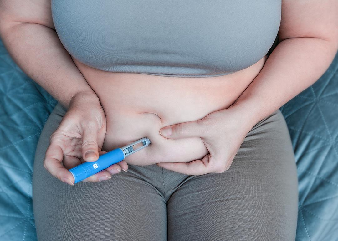 An overweight woman pinching belly fat to inject a GLP-1 pen on her stomach.