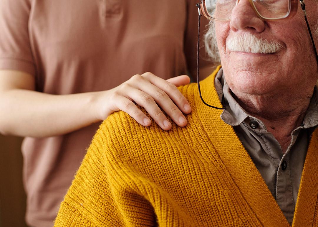 A young adult patting the shoulder of an elderly person as care and support.