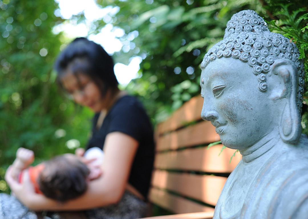 A Buddhist mother carrying and feeding her child outside in a park.