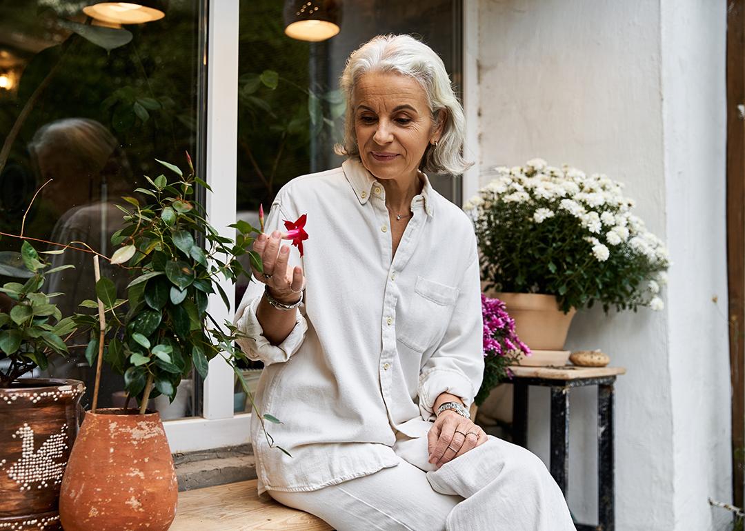 A senior woman sitting in her garden and looking at flowers.