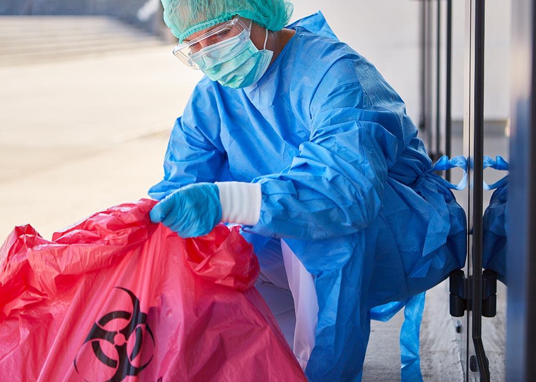 A cleaning staff in full safety gear carefully disposes biohazard waste in a clinic.