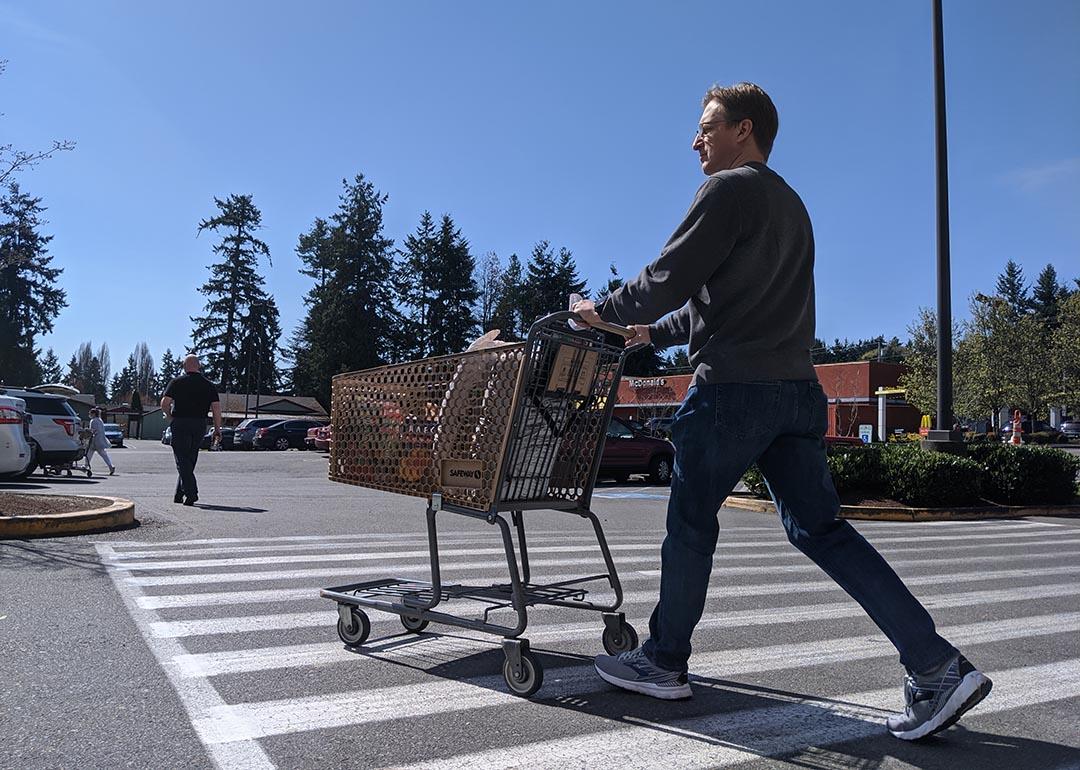 Street view of a man leaving with a supermarket with a grocery cart.