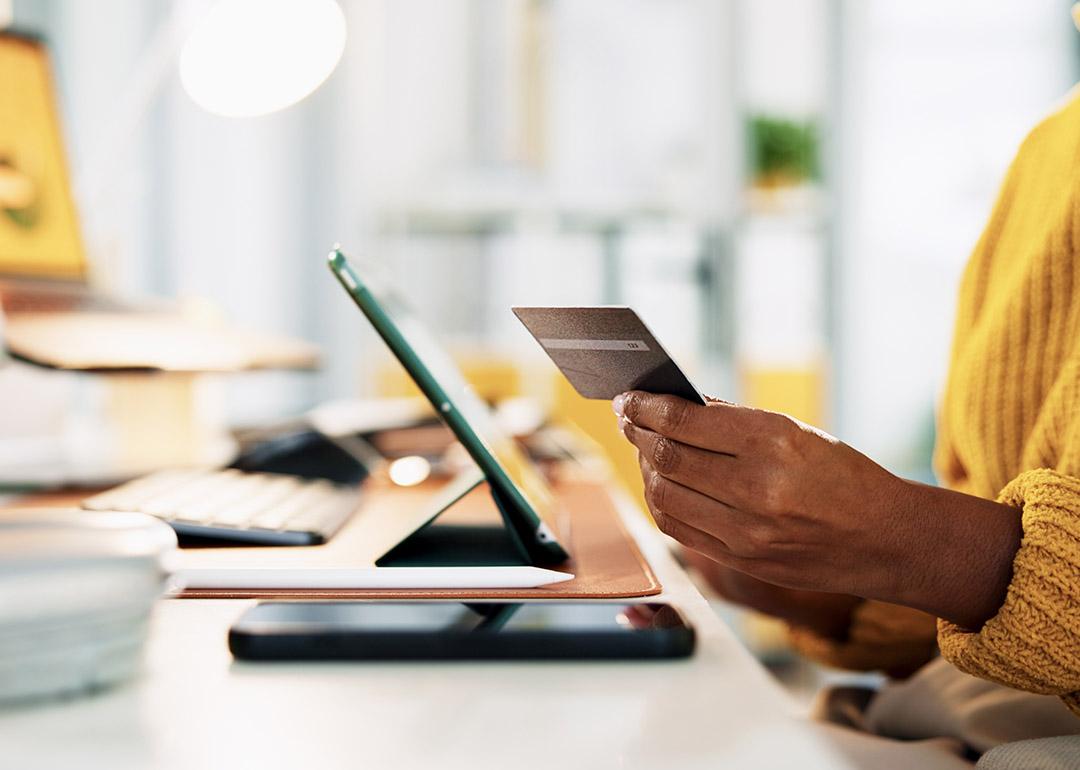 A business manager holding a credit card while checking digital transactions from a tablet. 