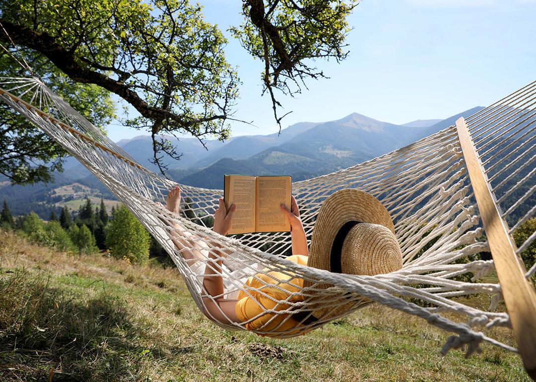 A person reading a book while relaxing in a hammock outdoors.