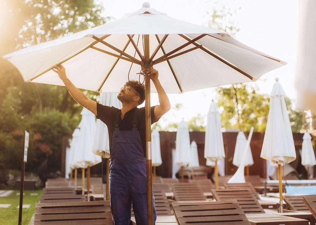 A hotel officer setting up a parasol beside the hotel's pool before guests' arrival.