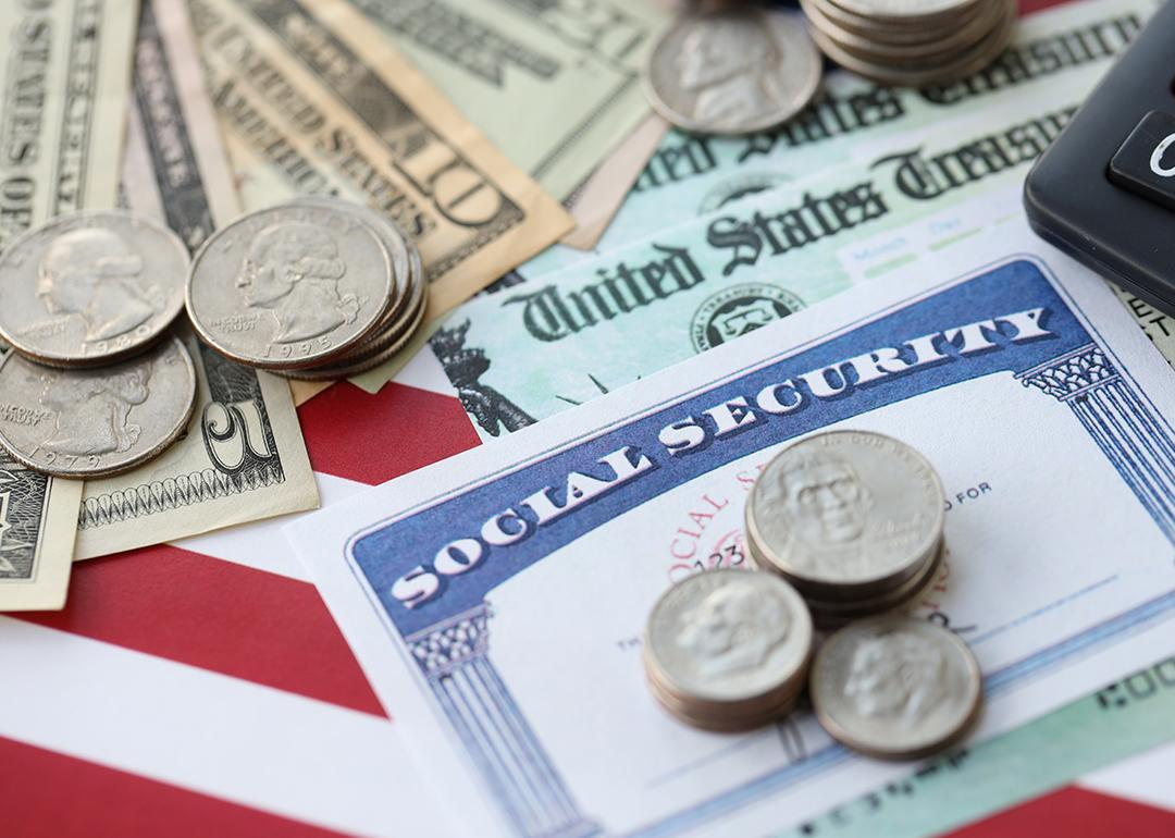 US dollar banknotes and coins, a social security form, and calculator on top of a US flag.