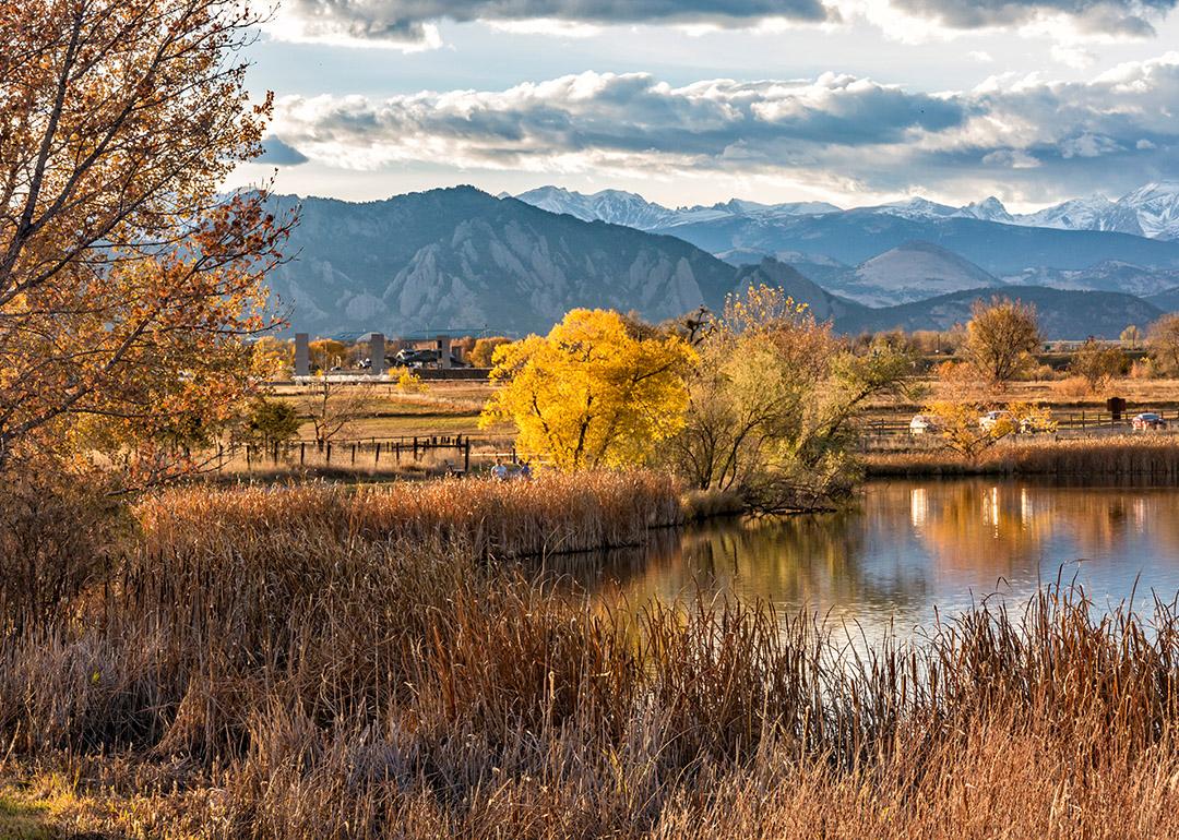 Flatirons and mountain ranges seen behind the Stearns Lake in an autumn landscape in Broomfield, Colorado, USA.