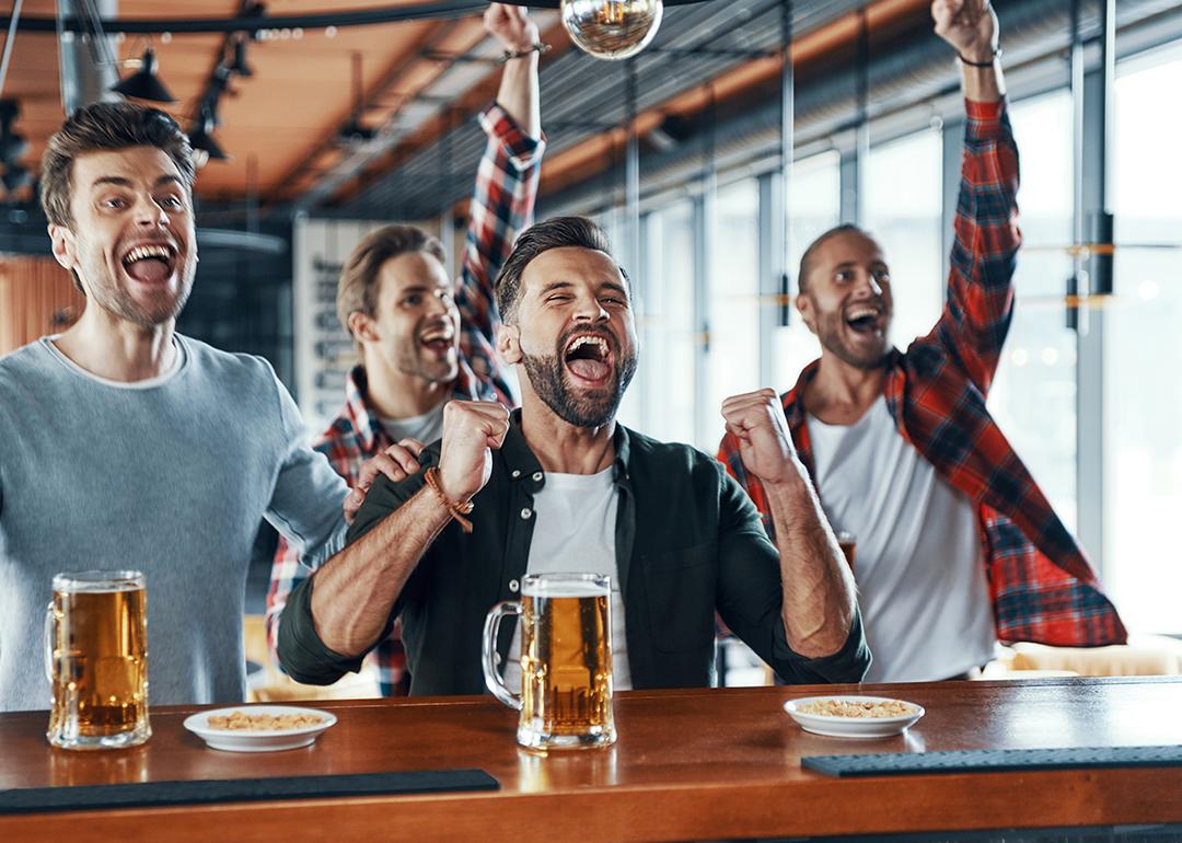 A group of men cheering and drinking beer while watching a sports game.
