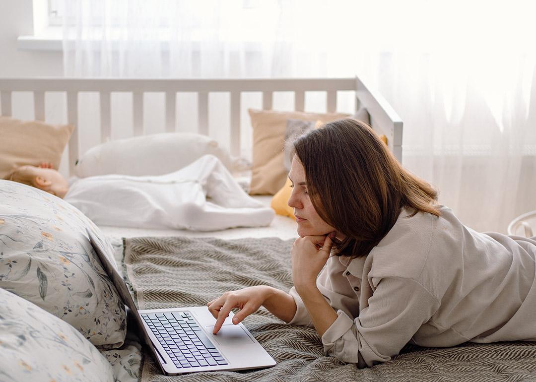 A parent working remotely from a bedroom while her baby toddler is sleeping in a crib.