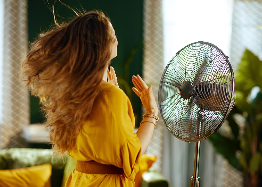 A woman with long hair enjoying the breeze from an electric standing fan.