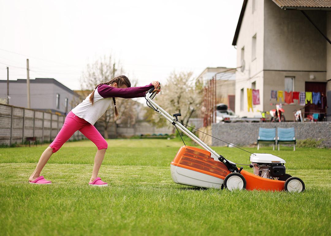A teenager pushing an electric lawnmower in their backyard during a summer holiday.