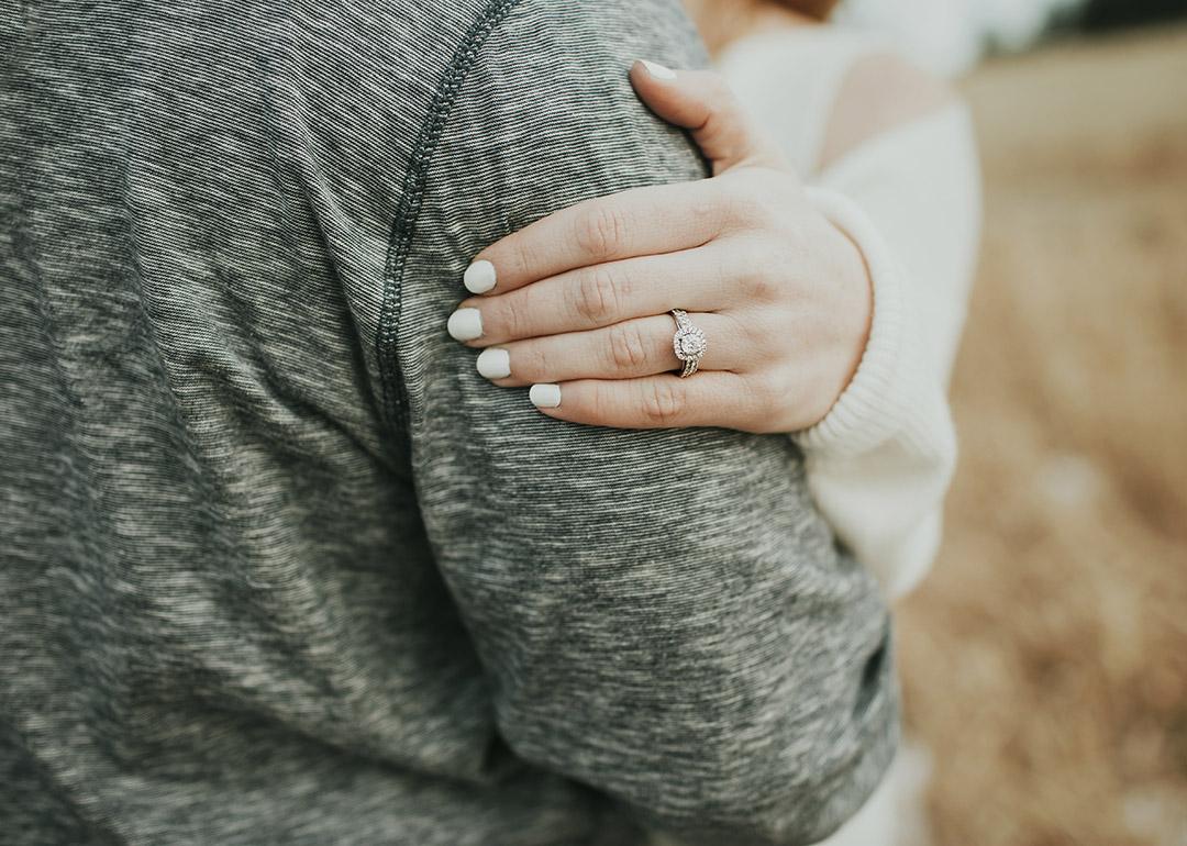 A diamond engagement ring on a woman's hand resting on her fiancé's arm.