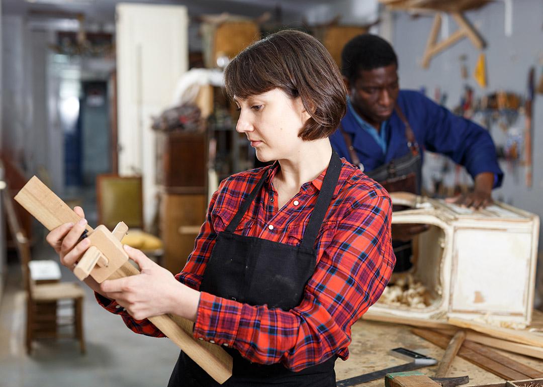 An artisan checking a wood component during a creation process of its furniture in a workshop.