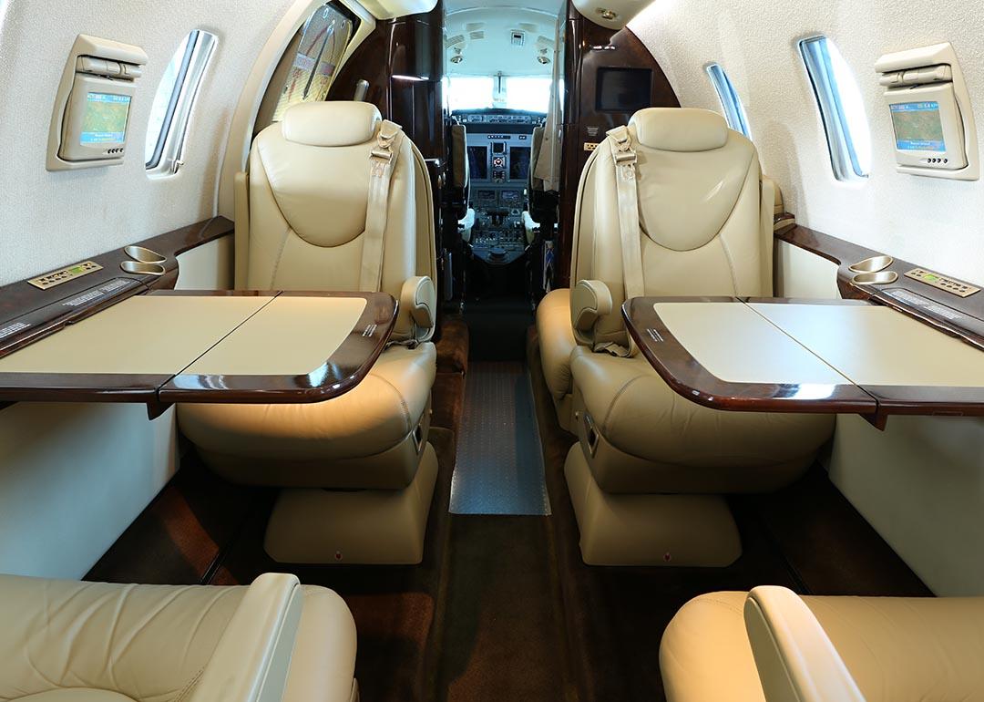 A private business jet cabin with open tables on both sides and lowered armrests.