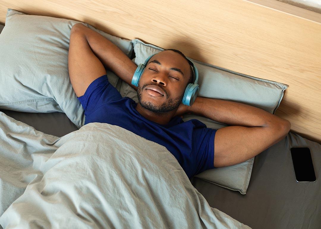 Man lying in bed with his hands on his head and wearing headphones.