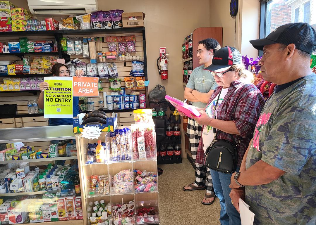 A store worker showing a "No warrant, No entry" / "Private area" signs behind the counter.