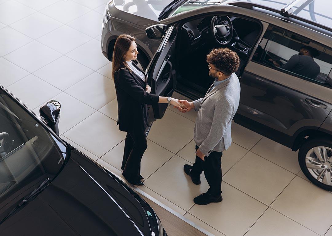 A car sales agent and a customer shaking hands after closing a deal in a car dealership shop.