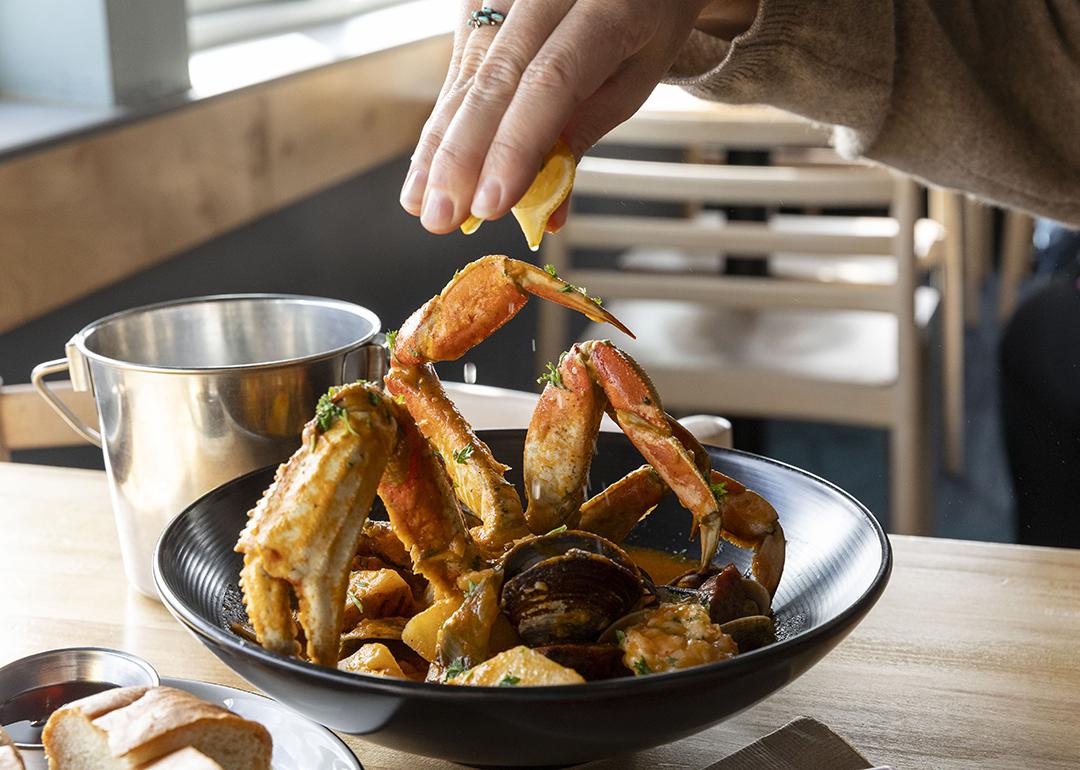 Person squeezing a slice of lemon over a crab dish.
