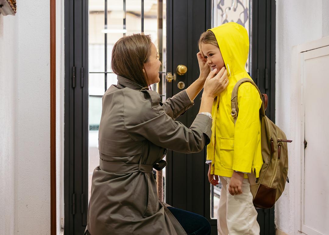 A mother preparing her child to go to school with a raincoat.