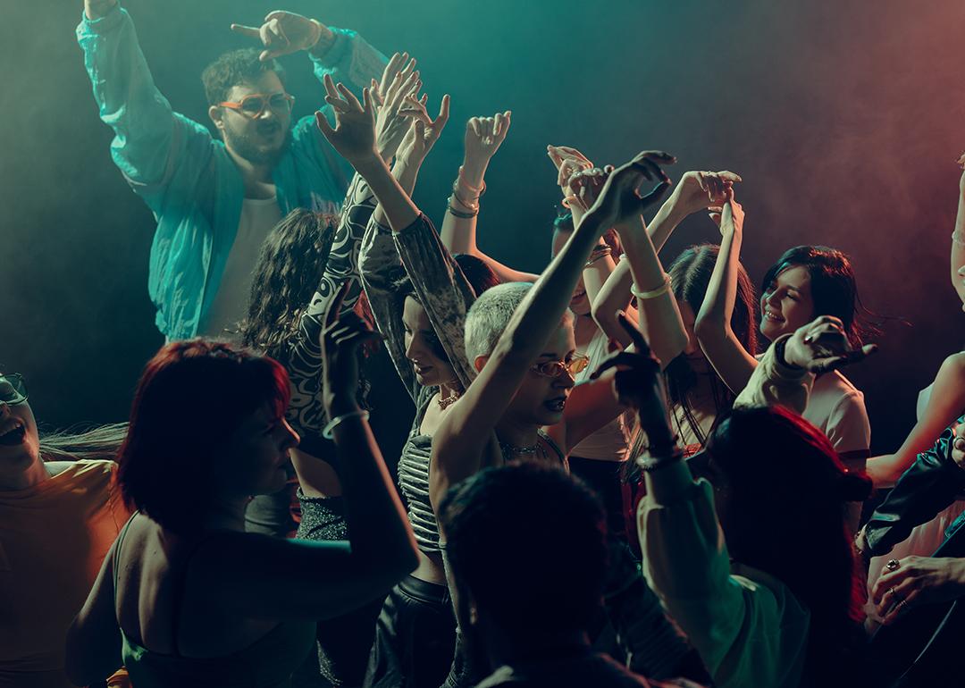 A crowd raising their hands as they dance under the lights in a club.