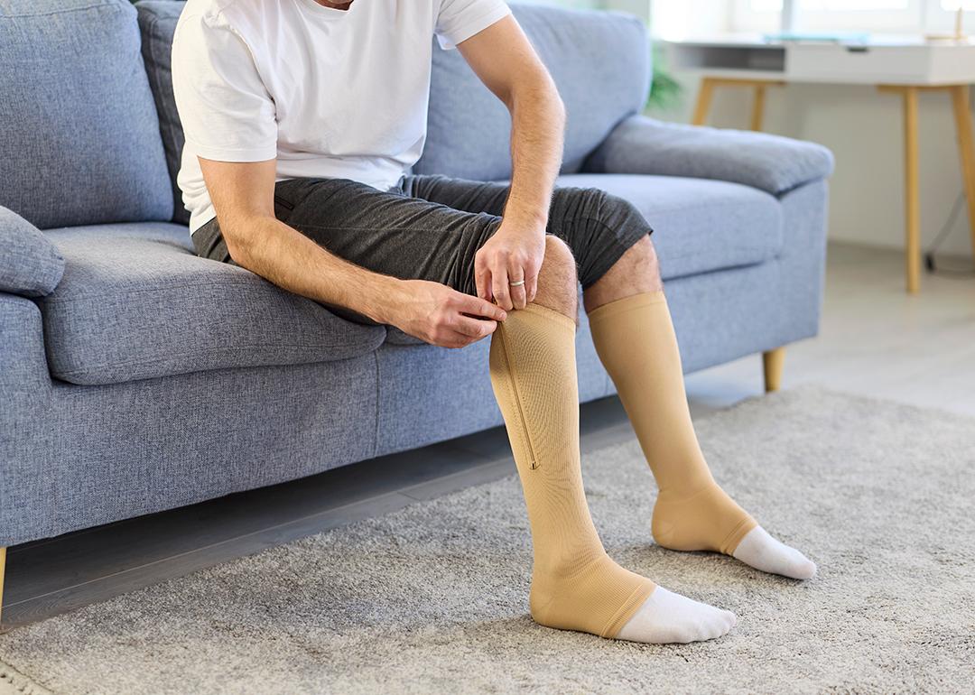 A man putting on knee-high compression stockings at home.