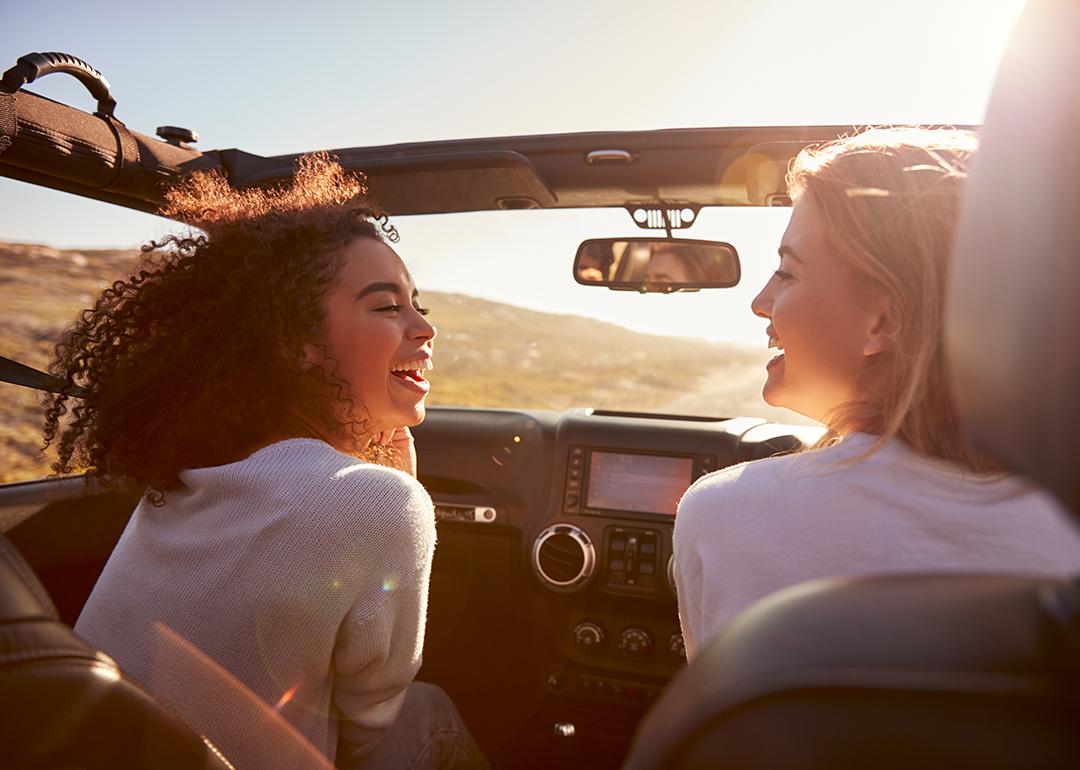 Two female friends happily riding on a highway in their convertible car.