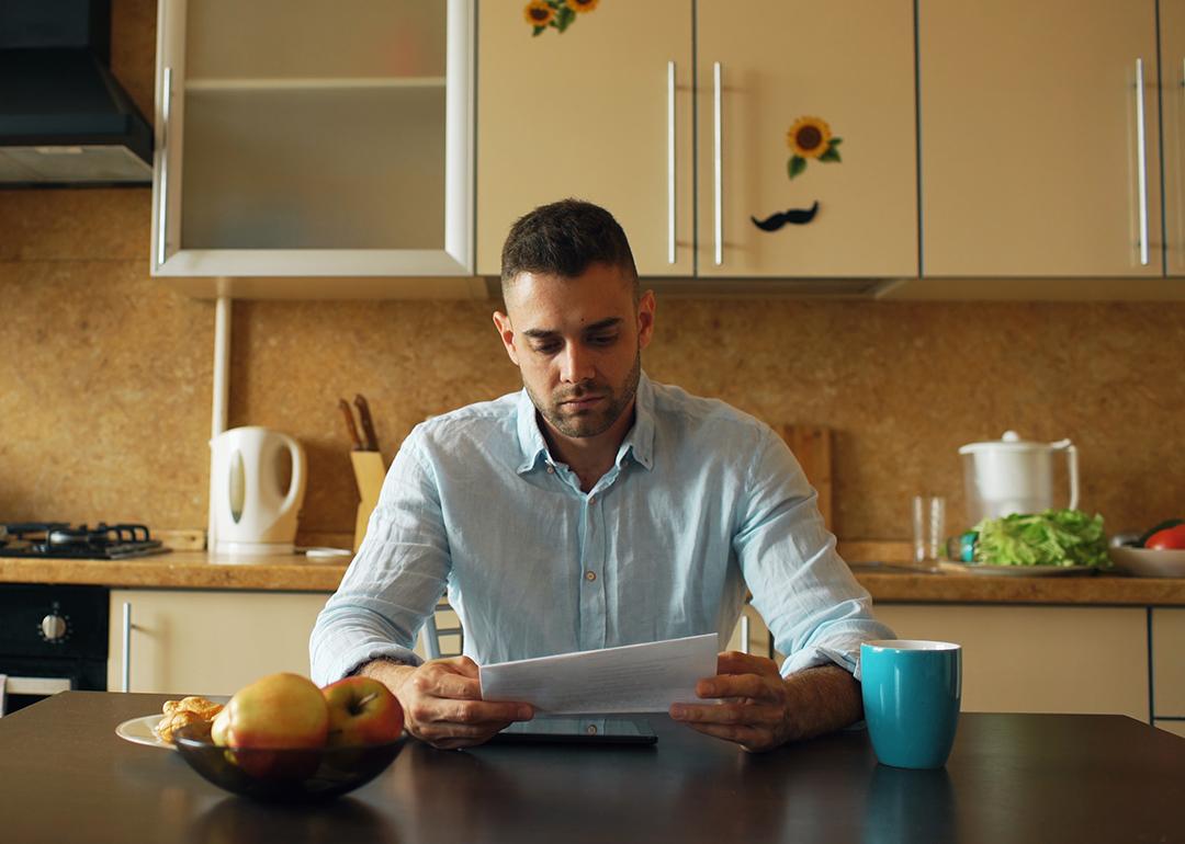 A male homeowner reading an unpaid bill letter in his kitchen.