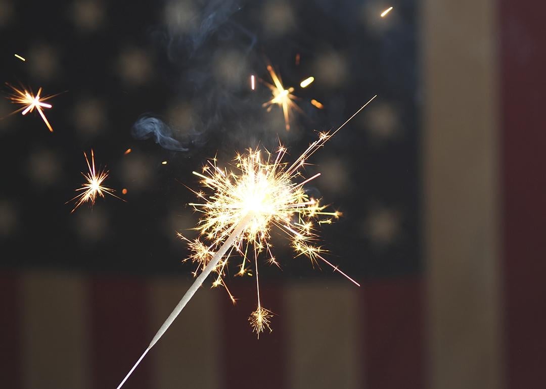 A sparkler firework with the US flag in the background for the 4th of July celebrations.